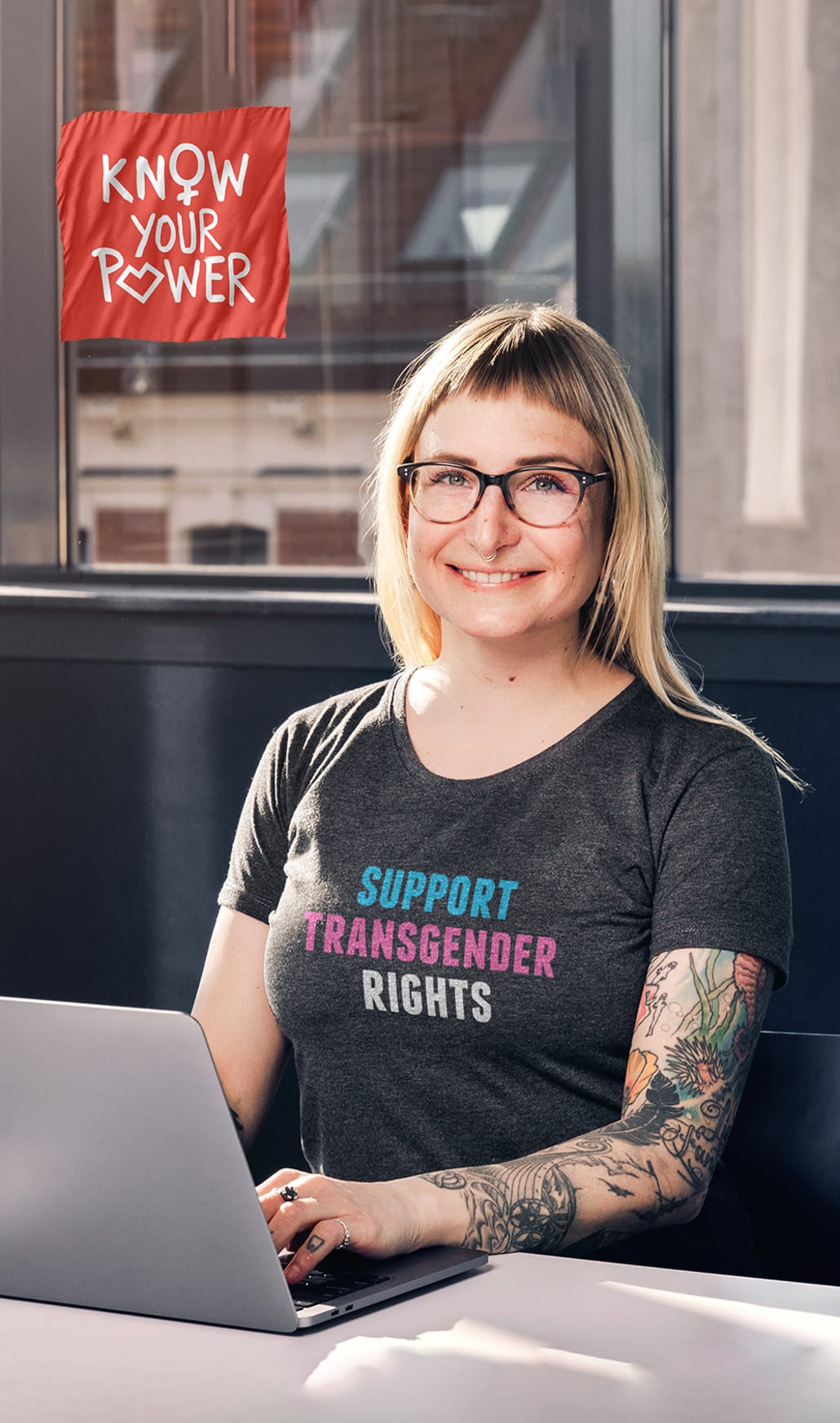 Sanja am Computer sitzend in grauem T-Shirt mit Motiv: support transgender rights